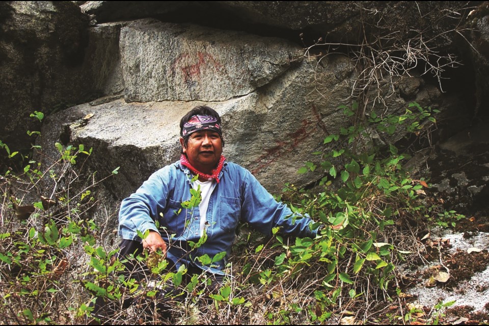 Retired Lil’wat cultural technician Johnny Jones posing with a pictograph depicting a moose and three goats. 
