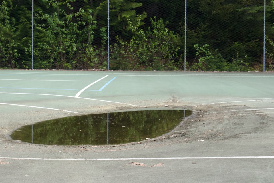 Slumping into itself from two sinkholes and discoloured by water damage, Taluswood Park tennis courts sit in disrepair behind a locked fence.