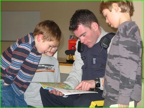 Const. Devon Jones reads to Spring Creek Elementary School primary students as part of Family Literacy Day celebrations January 27. Eleven readers, including storytellers who read in English, French and Japanese, shared their love of books with primary students while six writers worked with intermediate students to develop their technical and creative writing skills. From left to right Brett Hennessey, Brody Hennessey and Evan Low listen to Jones read from his childhood favorite The Pokey Little Puppy. Photo by Vivian Moreau