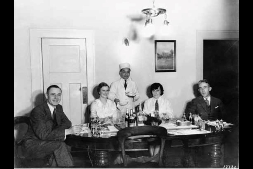 Two men and two women being served dinner by a Chinese chef at a guest house in Townsite on May 31, 1937.

