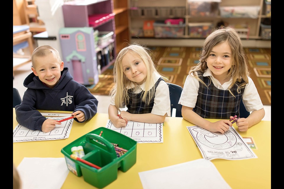 CLASSROOM WORK: Assumption School kindergarten students [from left] Luca Andreae, Beckette Robert and Jaelynn Bordignon complete a literacy task on the letter “Q”. The school is celebrating its 60th anniversary in early June, with several different celebrations planned.