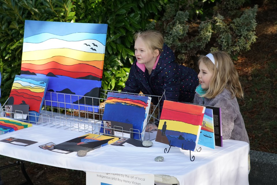 ESSENTIAL COMMODITY: Henderson Elementary School student Annabelle Wilson [left], grade two, and Aria Wadden, grade one, were at the sales table for works inspired by indigenous artist Roy Henry Vickers. The grade one and two class had been studying water and decided to put together a fundraising activity to raise awareness and provide funds for improving water access.