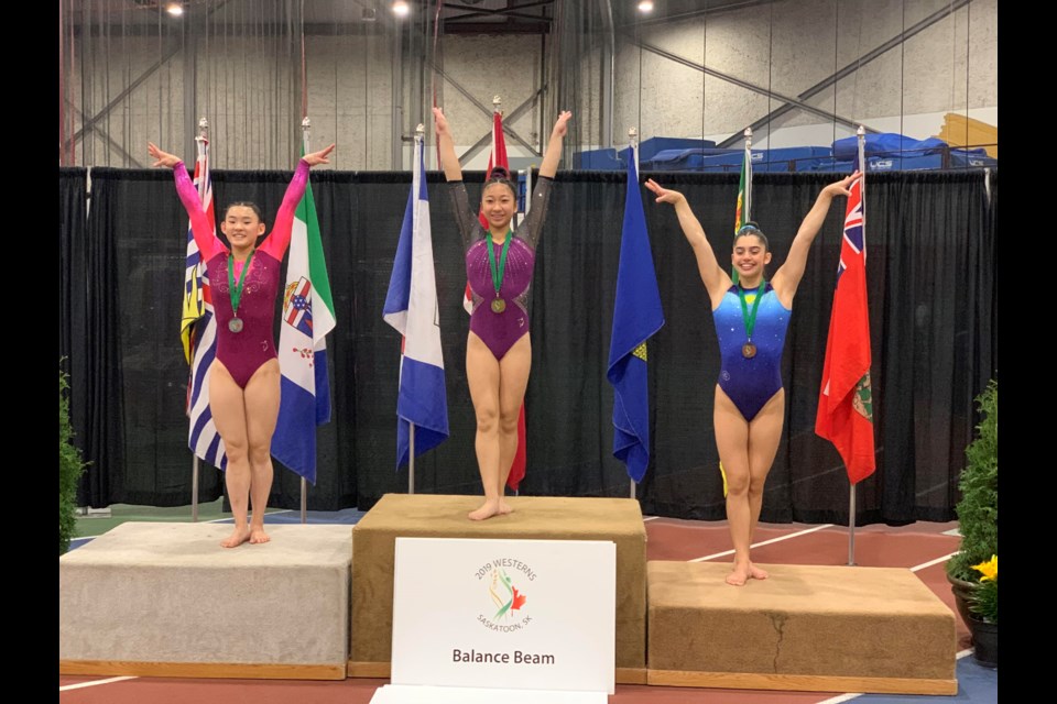 Alia Wilson (left) of Prince George lifts her arms with a smile on her face after winning a silver medal at the 2019 Western Canadian Championships (via Prince George Gymnastics)
