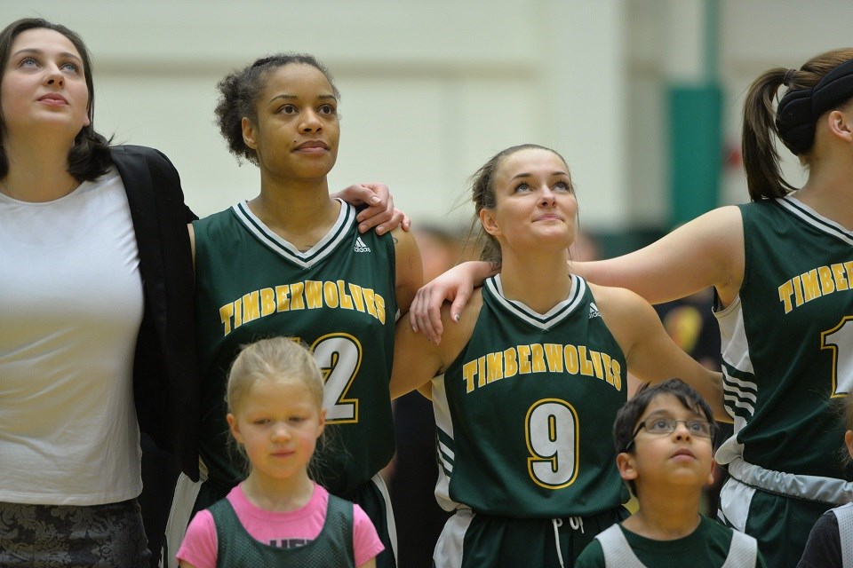 Maria Mongomo (2nd left) and Emily Holmes stand together with the UNBC Timberwolves at home against the MacEwan Griffins (via UNBC Athletics)