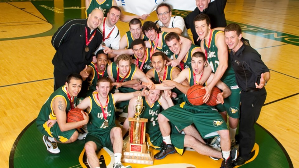 The 2010 UNBC Timberwolves men's basketball team shows big smiles in posing with the CCAA national championship trophy on their home court.