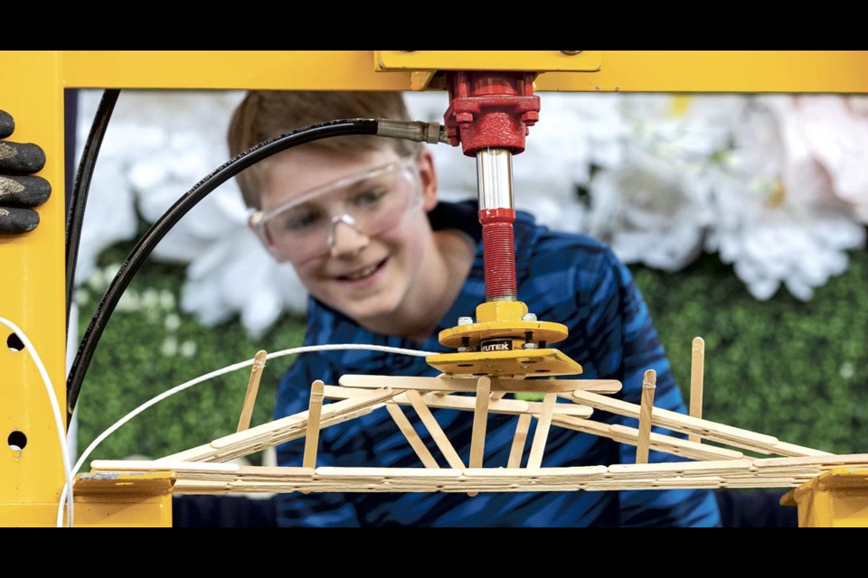 Levi Bartsch, 12, smiles as he watches his bridges start to collapse under the 144.9 load applied to it in the 25th Central Interior Popsicle Stick Bridge Building Contest Saturday, April 5, 2025 at Pine Centre Mall.