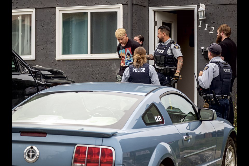 RCMP escort a man in handcuffs, suspected to be involved in an incident that saw two cyclists hit by a truck on Ospika Boulevard, from a residence at 112-101 Tabor Boulevard on Monday, July 7, 2025.
