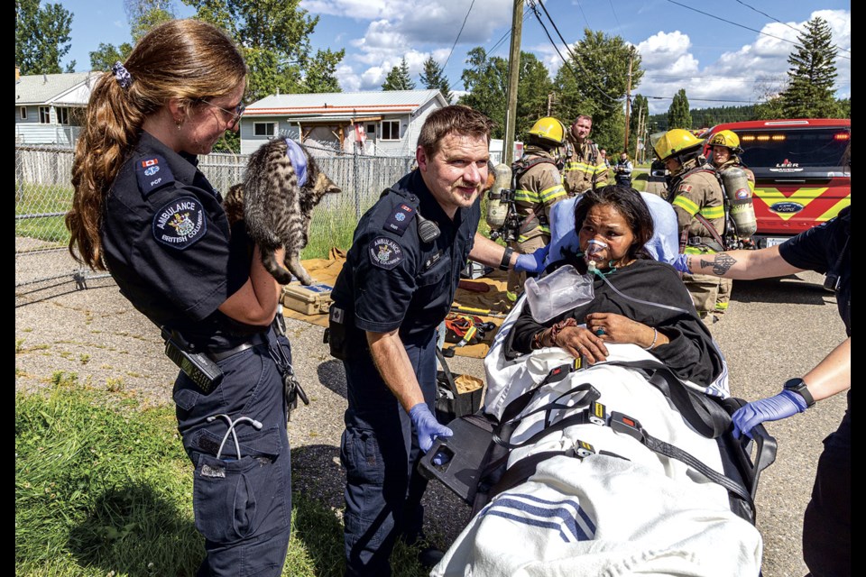 BC Ambulance Service Paramedics prepare to transport a victim of smoke inhalation following a duplex fire at 1411 Strathcona Avenue Friday, July 25, 2025 while another paramedic enquires if the two cats rescued from the building belong to the victim.