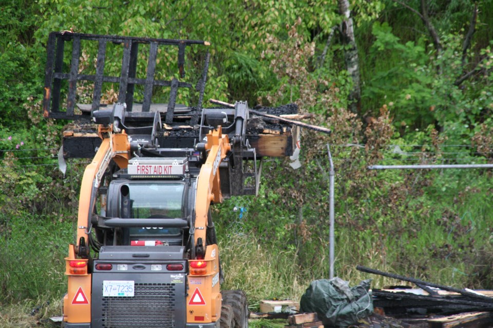 A worker uses a skid steer to clean up the debris left by the most recent fire at one of the temporary tiny homes in Moccasin Flats on Wednesday, June 12, 2024 in Prince George, B.C.