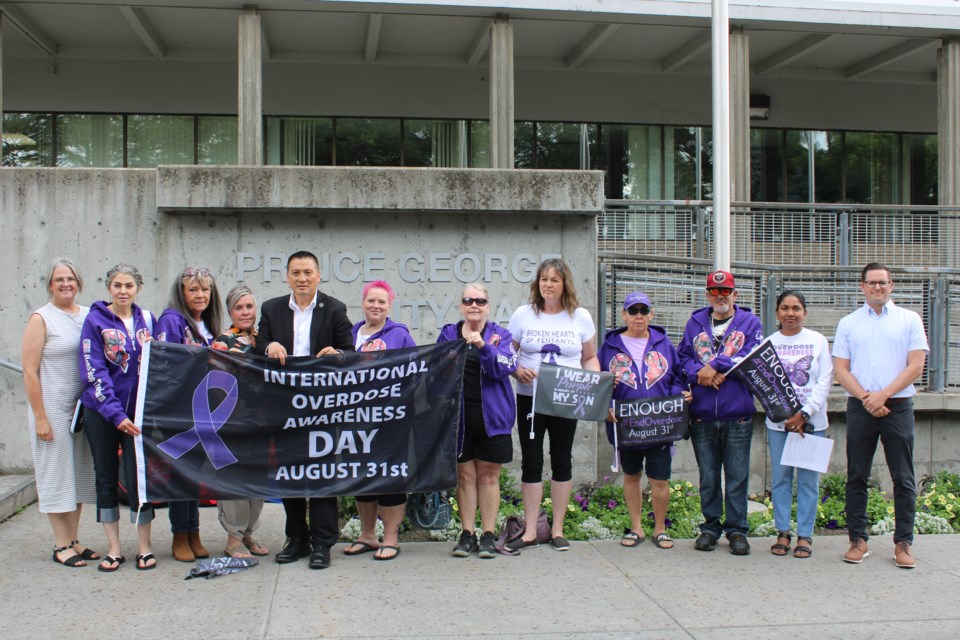 Mayor Simon Yu and Prince George-Mackenzie MLA Kiel Giddens, along with members of Broken Hearts of Fentanyl and Moms Stop the Harm, pose with the flag that is now over city hall on Friday, Aug 1, 2025 in Prince George BC.