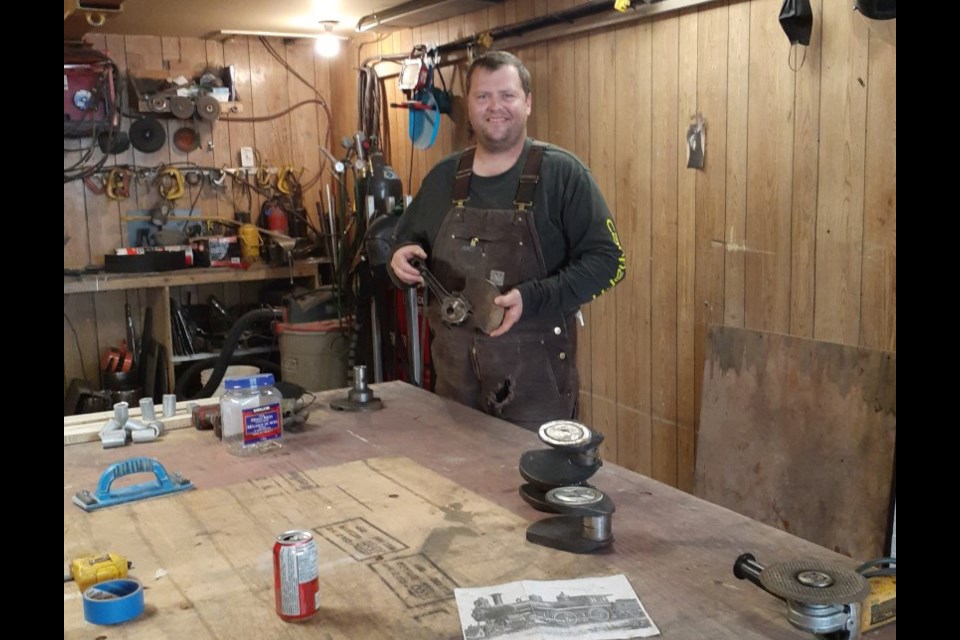 Local welder Brad Hutton is seen in the shop holding parts still to be put on the small-scale steam train he created during his leisure time during the pandemic.