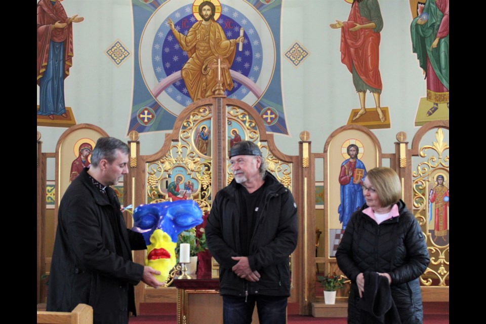 Father Andrii Chornenkyii of St. George's Ukrainian Catholic Church, left, accepts an art piece created by renown local artist Elmer Gunderson, as MLA Shirley Bond looks on Friday morning at St. George's Church.