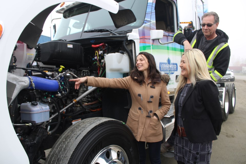 Hydra Energy CEO Jessica Verhagen points out the fuel injection system used to deliver hydrogen fuel to the engine of a long-haul truck as Lodgewood Enterprises president Arlen Gagne and truck driver Percy Hurd look on.