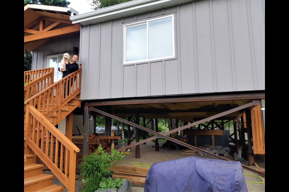 Emma Broomsgrove and her dog Birdy stand outside the front entrance of their Farrell Street home in South Fort George while in the background the flooding Fraser River breaks over its banks.