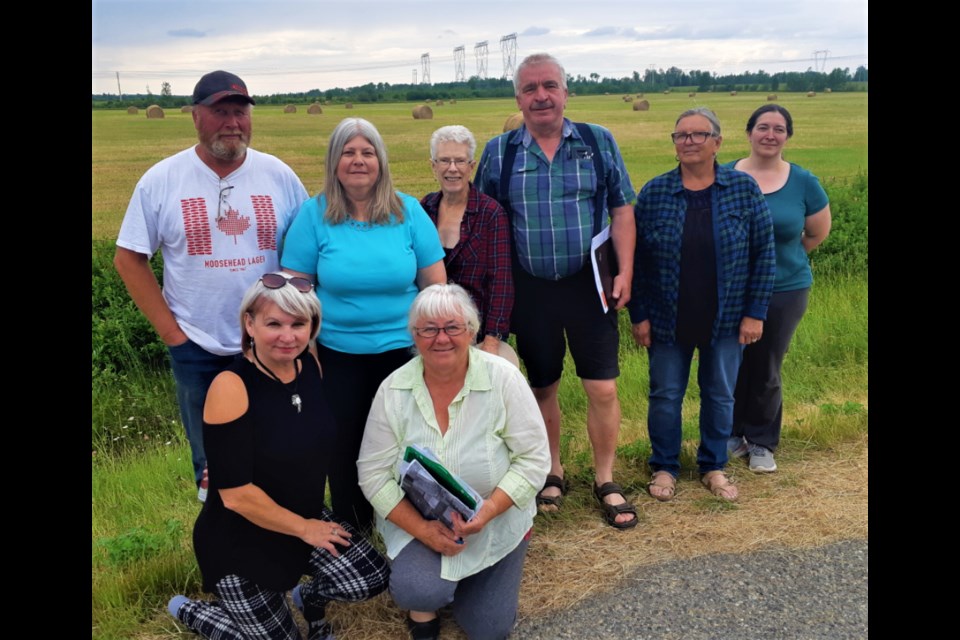 A group of Pineview residents who farm the land surrounding the site of a proposed petrochemical extractor to be built by West Coast Olefins Ltd., gathers in front of the proposed site in the background. From left, back row, are Gary Wood, Carol Wood, Marilyn Murray, Joe Cvenkel, Judith Wolfe and Sheila Lewis, crouching, from left, are Sharon Bonthoux and Lynn Gilliard. 