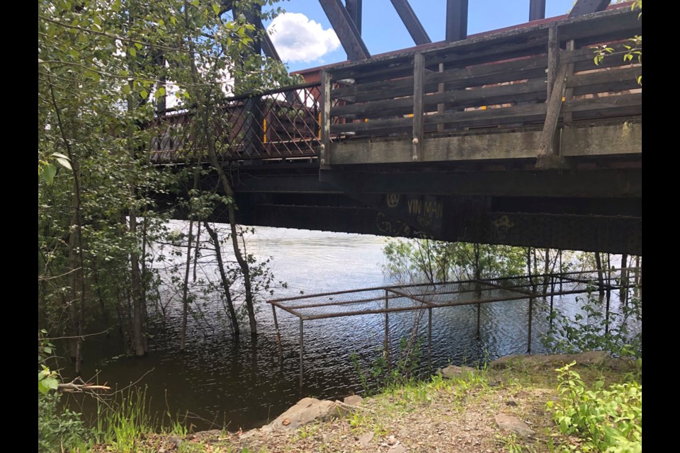 Water from the Fraser River has fully submerged the Heritage River Trail at the CN Rail bridge. The steel grate which protects trail users from falling debris can be seen jutting out from the river water.