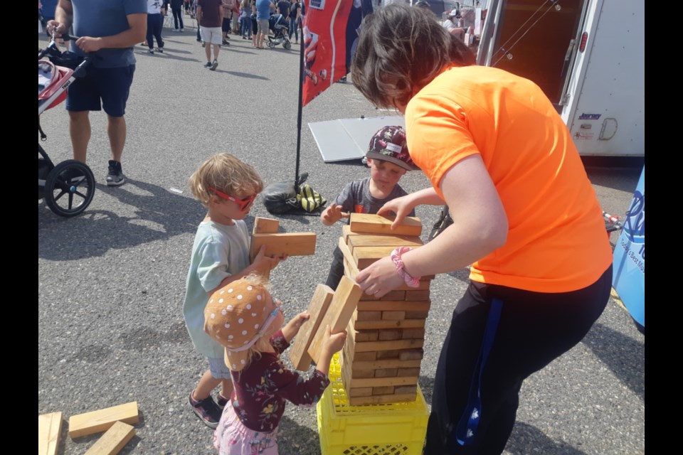Two-year-old Mila Thibault, left, and her four-year-old brother Sully pile on Jenga blocks while their three-year-old cousin Augi and CKPG Fun Chaser Alora Bowness add stability to the growing stack they built Saturday at Rooftop Rocks: Flatbed Edition.