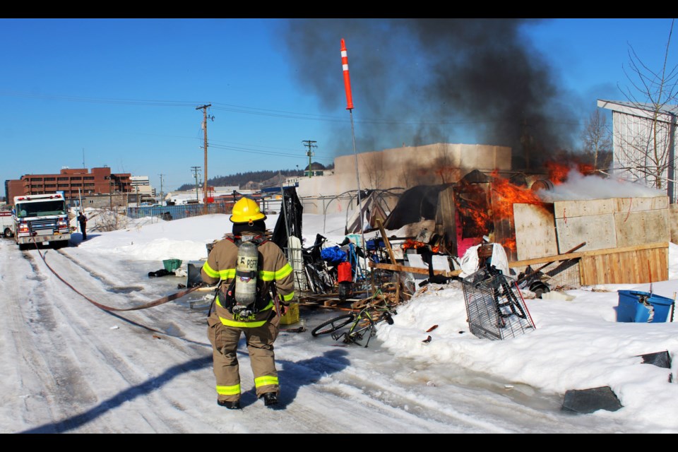 A firefighter drags his hose into position to fight a fire in the Moccasin Flats homeless encampment east of the downtown core.