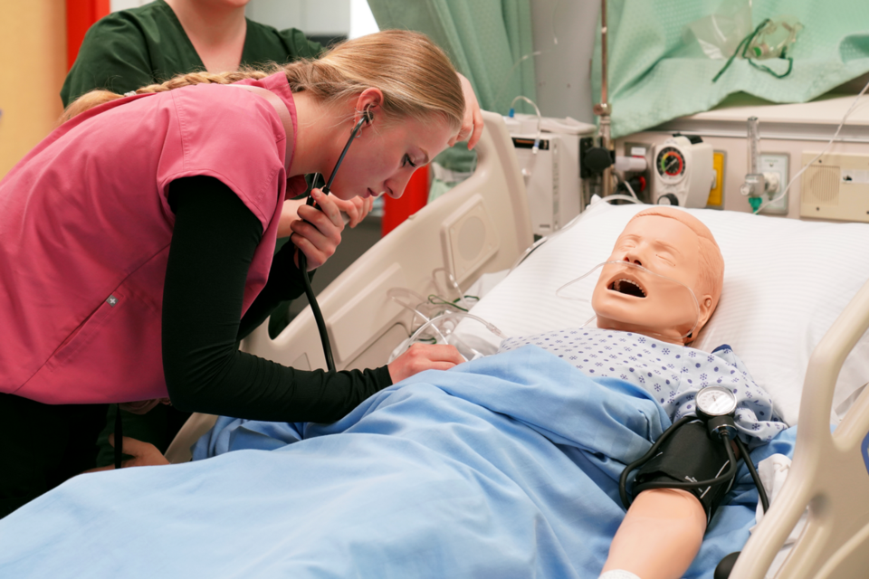 A College of New Caledonia nursing student checks vital signs on a patient simulator manikin used for training.