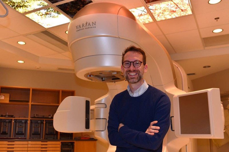 Dr. Rob Olson stands in front of a linear accelerator at the BC Cancer - Prince George centre; the machine is used to deliver SABR treatment to clinical trial patients.