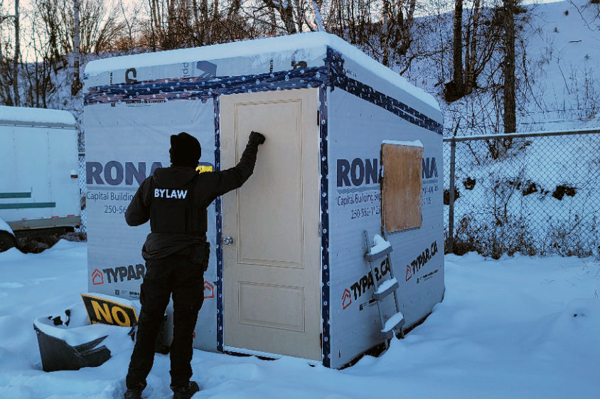On a chilly Thursday morning bylaw services officer Braeden Rumming knocks on one of the structures that house residents of the Moccasin Flats homeless encampment on the east side of downtown. The city posted signs warning residents of the hazards of living in unapproved shelters on the site.