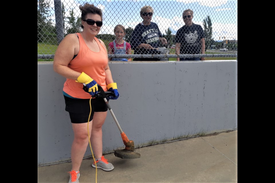 Tammy Scott takes care of some weeds sprouting through the concrete floor of the Carney Street lacrosse box during Saturday's work bee,. Standing behind the fence are, from left, Tammy's granddaughter Rylee, her mom Pat and her sister Lisa. The facility at the corner of Carney Street and Massey Avenue will eventually be renamed the Glen 'Moose' Scott Lacrosse Box.