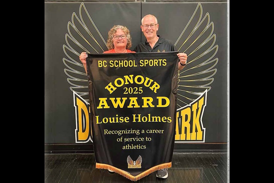 Louise and Dave Holmes hold the BC School Sports Honour Award banner she received Wednesday, June 24, 2025, in recognition of her career commitment to school sports at Duchess Park Secondary School. The banner will be hung next to the provincial championship athlete banners at Duchess Park gym.
