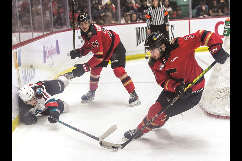 Prince George Cougars defenceman Ephram McNutt scoops the puck from fallen Kelowna Rockets forward Ethan Neutens after he was knocked down against the boards by Keaton Dowhaniuk (24) during the first period of Game 2 at CN Centre Saturday.

