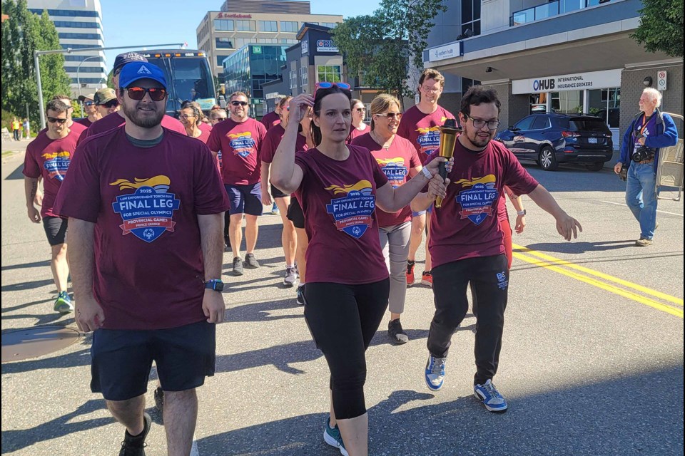 RCMP Cpl. Jennifer Cooper and Cariboo- North East track and field athlete Spencer Rourke carry the flame in the Law Enforcement Torch Parade on Wednesday, July 9, 2025. The parade, the first event of the BC Special Olympics Summer Games, started on Victoria Street and led to CN Centre.