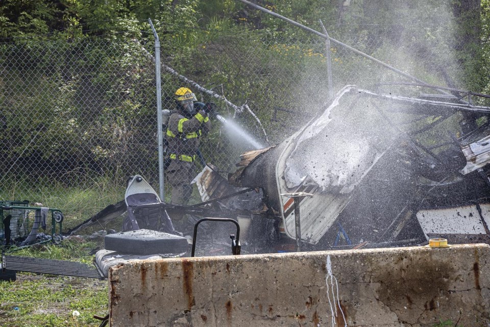 A firefighter from Prince George Fire Rescue Engine-52 blasts water deep into the depths of a still-smouldering trailer at Moccasin Flats shortly after 3 p.m Sunday, May 25, 2025. No one was injured in the fire and the fire truck stayed to make sure the blaze was completely extinguished.