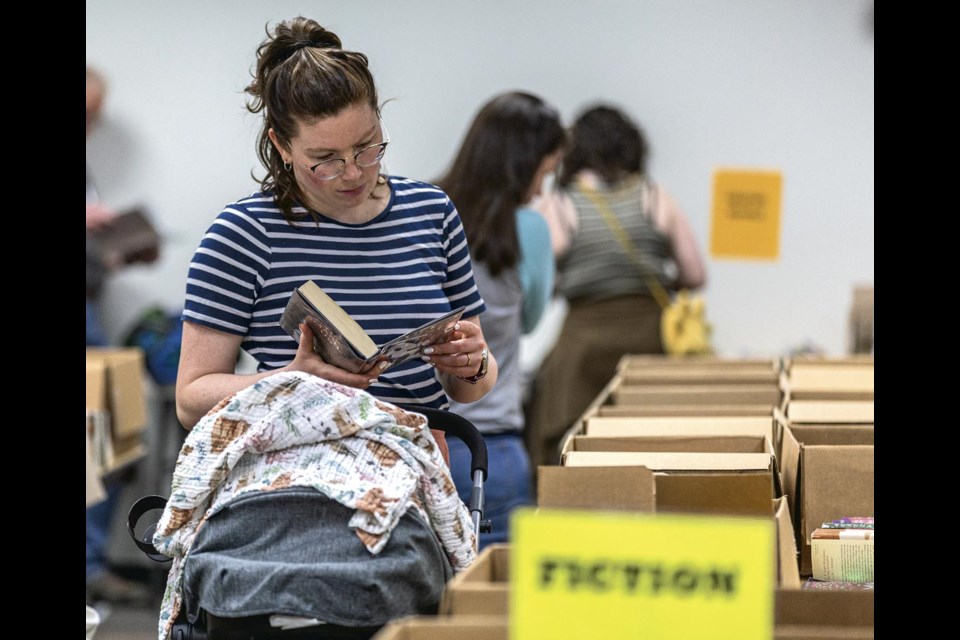 Julie Forrest, accompanied by two-and-a-half-month-old Charlotte, takes an exploratory read of a promising book at the Friends of the Library Spring Book Sale at the Bob Harkins Branch of the Prince George Public Library Friday, April 25, 2025. 