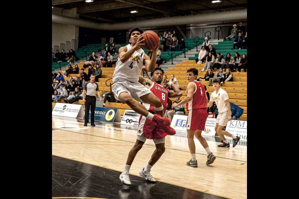 The UNBC Timberwolves' Isaiah Bias jumps around Calgary Dinos' Noah Wharton as he crosses the key to the basket in an exhibition game at Brownridge Court Friday night.