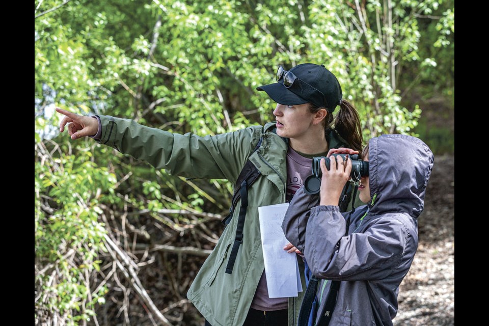 Cara Snell, a UNBC PhD candidate and vice-president of Prince George Naturalist Club directs Adam Jones, 10, where to look through the binoculars to watch a pair of Bufflehead Ducks at the confluence of the Nechako and Fraser rivers on Saturday, June 1, 2024 in Prince George, B.C. Snell was leading a bird walk through Cottonwood Island Park as part of the Walk PG Outdoor Festival.
