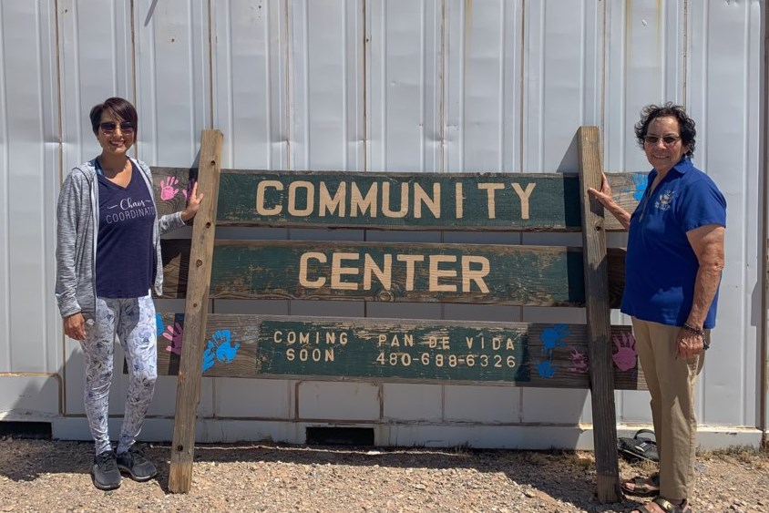 Pan de Vida founder Mary Gloria, right, and her daughter Kelly, left, stand outside one of the shipping containers holding various donations and the sign for community center they're getting ready to develop on the one-acre plot of land they own in San Tan Valley.