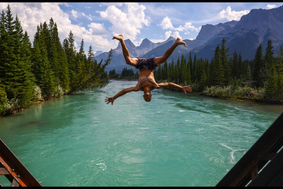 Jamie Muller performs a stylized back flip from Engine Bridge into the Bow River on Saturday, Aug. 1, 2020. Environment Canada issued heat warnings for Banff National Park, Canmore, MD of Bighorn and Kananaskis Country, stating temperatures were expected to reach or exceed 29 C with overnight lows near 14 C. EVAN BUHLER RMO PHOTO⁠