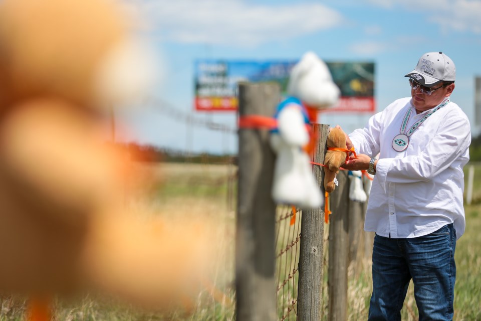 Chris Goodstoney a member of the Wesley Band of the Stoney Nakoda First Nation ties one of 215 teddy bears, in memory of the 215 children found in a mass grave on the grounds of the Kamloops Residential School, to a fence along the Trans-Canada Highway near the Stoney Nakoda Resort Casino on Tuesday (June 1). EVAN BUHLER RMO PHOTO