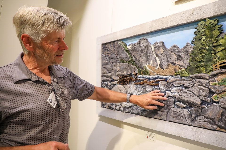 Clarence Durocher explains the dynamic flow of water using epoxy in front of his works at the Canmore Art Guild July exhibit on Sunday (July 10). JUNGMIN HAM RMO PHOTO