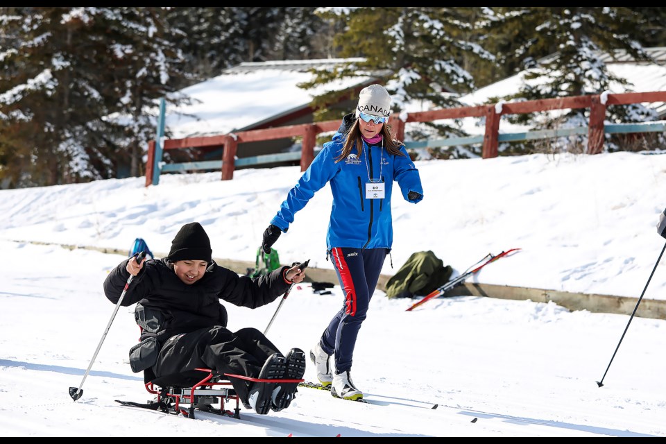 Under the coaching of Brittany Hudak, a Paralympic bronze medalist and Nordic ski instructor at Rocky Mountain Adaptive, Athena Twoyoungmen, left, of Nakoda Elemental School experiences adaptive bi ski in the Spirit North community festival at the Canmore Nordic Centre on Wednesday (March 15). JUNGMIN HAM RMO PHOTO