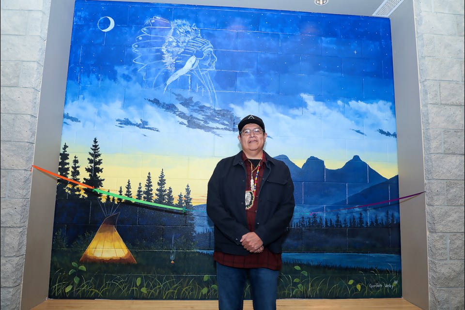 Îyârhe (Stoney) Nakoda artist Gordon Wesley poses in front of his mural at Canmore Civic Centre on Thursday (June 15). JUNGMIN HAM RMO PHOTO