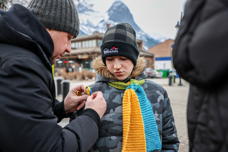 Serhii Sheiko, left, puts a blue and yellow Ukrainian ribbon on his son Kirill Sheiko to mark the second anniversary of the war with Russia at Canmore Civic Centre on Saturday (Feb. 24). JUNGMIN HAM RMO PHOTO 