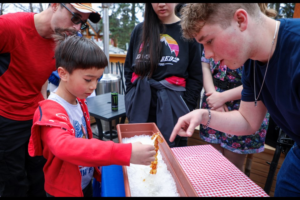 Finn Twomey, who is due to graduate in May, teaches Leo Sauvageau how to roll the maple taffy at the Sugar Shack at the fundraiser for the graduating class of École Notre-Dame des Monts (NDM) at Tavern 1883 in Canmore on Saturday (April 27). JUNGMIN HAM RMO PHOTO