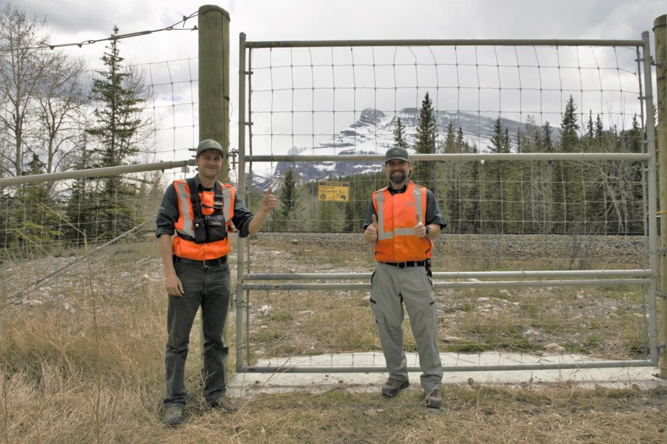 Parks Canada staff Peter White, left, and Chris Groves stand in front of a hotwire fence east of the Banff townsite in 2020. DAN RAFLA PARKS PHOTO