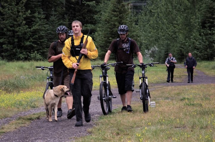 Conservation officer Brodie Rundel leads a group of cyclists from the end of the Highline mountain bike trail to the dog park following a cougar attack on their dog Monday