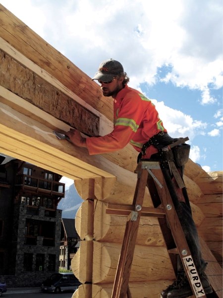 Matt Krimmer with Tyee Log Homes works on the replica Canmore Opera House, Friday (Aug. 26). A single log from the original structure can be seen inset above the doorway.