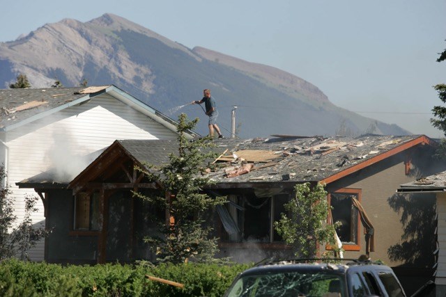 A homeowner uses a hose to spray water on his roof after a nearby house exploded in Canmore on Friday (June 26) afternoon.