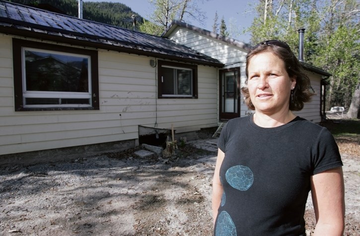 Sue Arlidge in front of her damaged Exshaw home one year after the flood.
