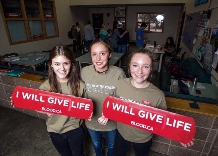 Student council members Leolinda Cocaj, Kyla Morrow and Brooke Anderson hold Canadian Blood Services signs outside a blood testing drive at Canmore Collegiate High School on