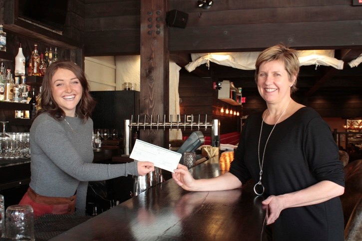 Banff Hospitality Collective commitment committee chair Kasper Millar, left, presents YWCA Banff CEO Connie MacDonald with funds raised by staff during the eight days of