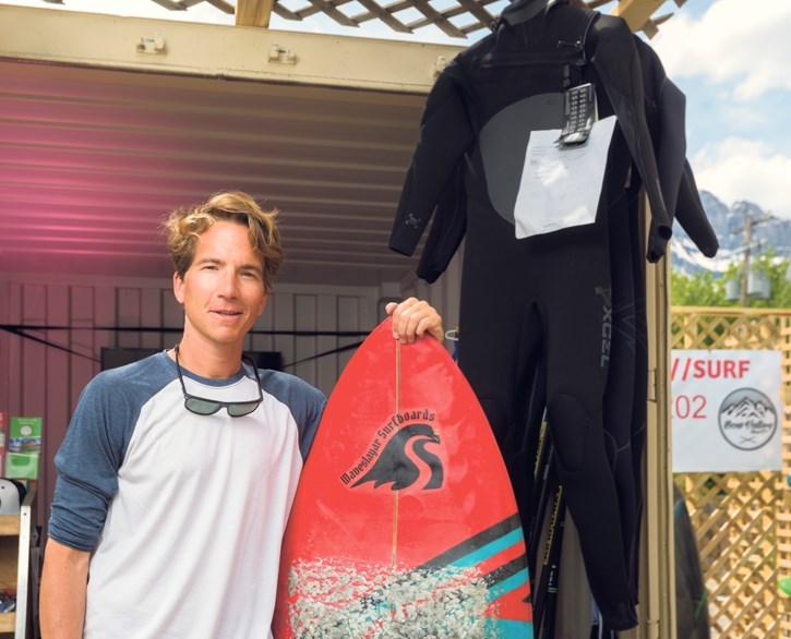 Brandon Olsthoorn stands with a surfboard at his pop up shop on Main Street in Canmore.
