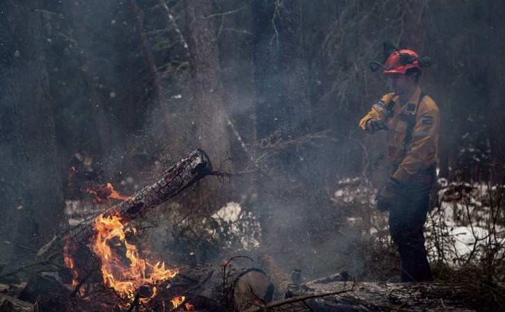 Parks Canada firefighter Matt Foster throws a log onto a FireSmart burn pile along the Fenland Trail in Banff on Thursday (Nov. 9). Parks Canada and the Town of Banff have